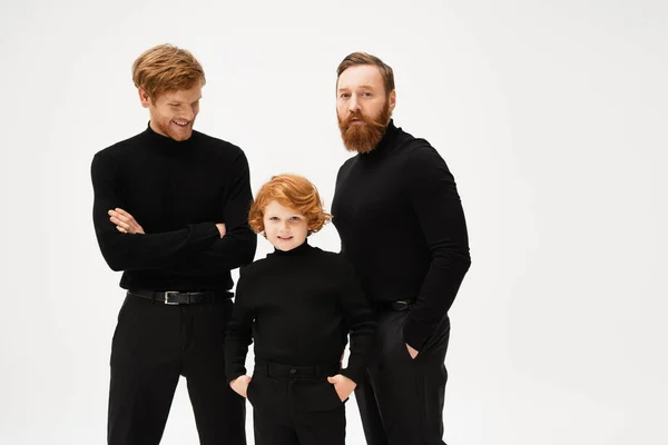 Bearded man looking at camera near redhead son and grandson posing in black clothes isolated on grey — Stock Photo