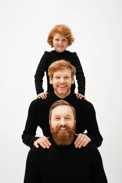Happy redhead boy and bearded men in black turtlenecks looking at camera while posing isolated on grey — Photo de stock