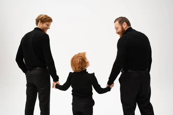 Back view of bearded men and red haired boy holding hands and looking at each other isolated on grey — Stockfoto