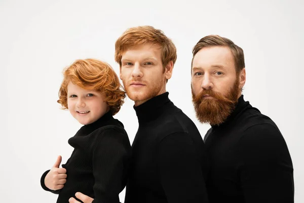 Bearded men in black sweaters looking at camera near happy kid showing thumb up isolated on grey — Foto stock