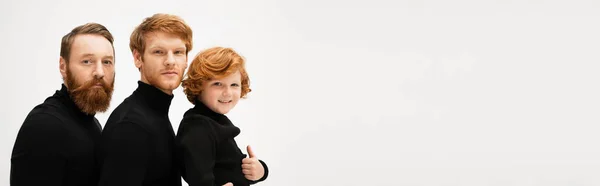 Happy red haired boy showing thumb up near bearded grandpa and father in black turtlenecks isolated on grey, banner — Stock Photo