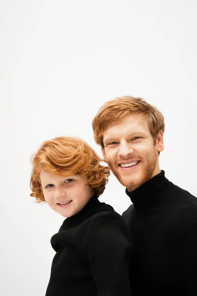 Family portrait of red haired father and son in black turtlenecks smiling at camera isolated on grey — Stock Photo
