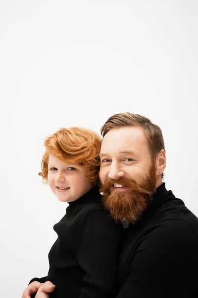 Happy bearded man and redhead grandson wearing black sweaters and looking at camera isolated on grey — Stockfoto