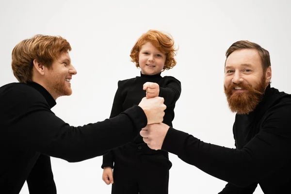 Happy bearded men and redhead boy in black turtlenecks joining fists isolated on grey — Foto stock