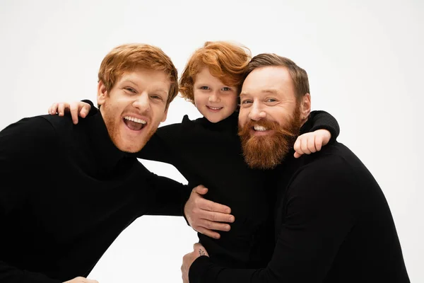 Excited man with happy redhead son and bearded dad embracing and smiling at camera isolated on grey — Stock Photo