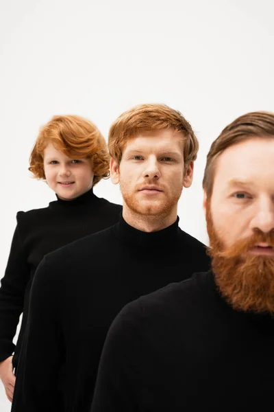 Smiling boy looking at camera near red haired dad and bearded grandfather in black turtlenecks isolated on grey — Stock Photo