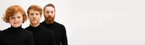 Redhead men in black sweaters looking at camera near happy boy isolated on grey, banner — Stock Photo