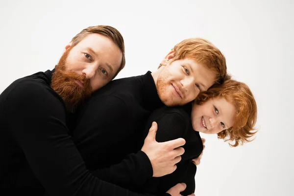 Щасливий бородатий чоловік обіймає рудого сина і онука в чорних светрах ізольовані на сірому — стокове фото