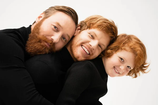 Family portrait of redhead bearded man with son and grandson smiling at camera isolated on grey — Stock Photo