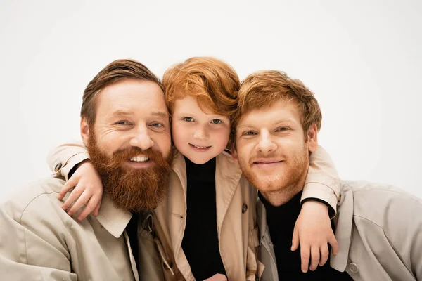 Family portrait of red haired boy hugging cheerful bearded grandfather and dad isolated on grey — Stock Photo