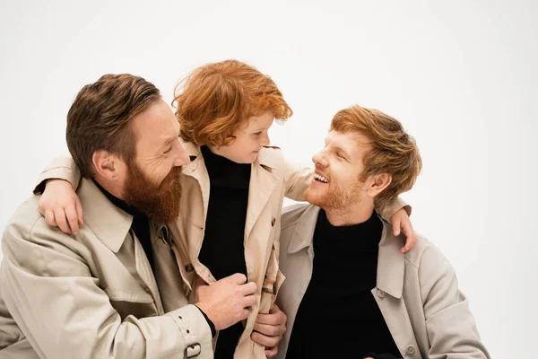 Bearded man smiling near cheerful son and grandson in trench coats looking at each other isolated on grey — Foto stock