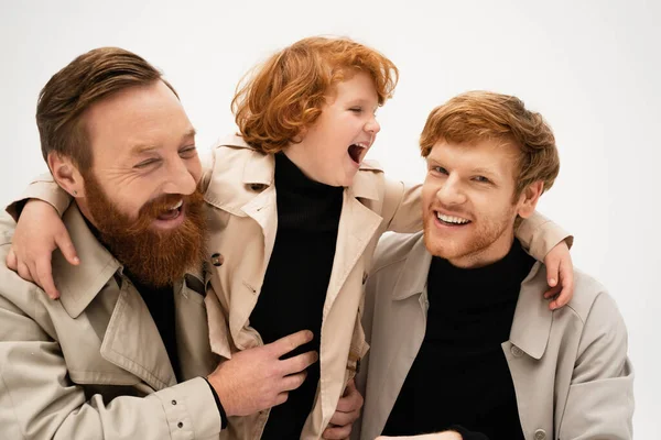 Excited boy laughing and embracing father and bearded grandpa isolated on grey — Stock Photo