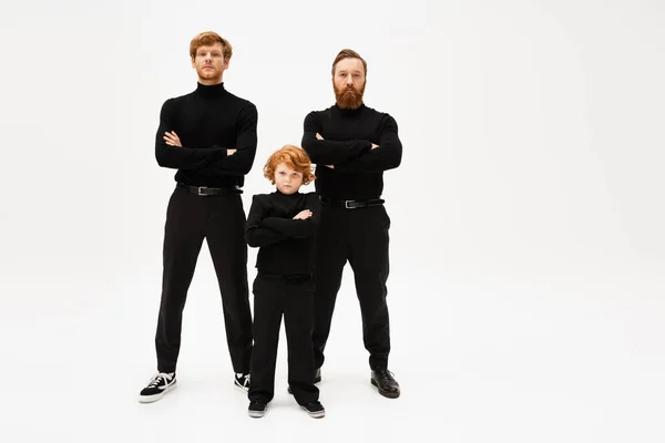 Full length of redhead men and boy in black clothes posing with crossed arms on light grey background — Stock Photo