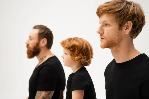 Side view of redhead boy near dad and bearded grandfather in black t-shirts isolated on grey — Stock Photo