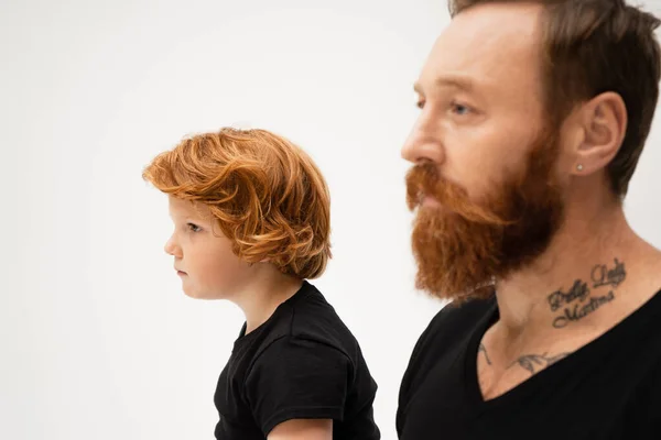 Side view of redhead boy in near bearded and tattooed grandpa on blurred foreground isolated on grey — Stock Photo