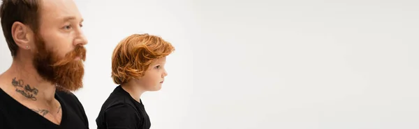 Side view of bearded tattooed man near red haired grandson isolated on grey, banner — Stock Photo