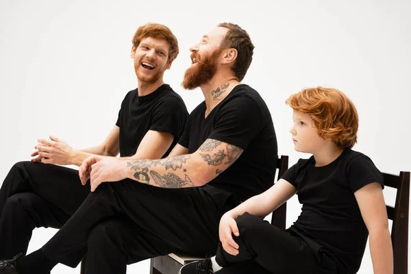 Redhead boy sitting near tattooed grandpa and dad laughing isolated on grey — Stock Photo
