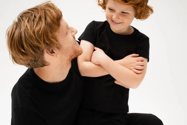 Cheerful boy with crossed arms looking at redhead father isolated on grey — Stock Photo
