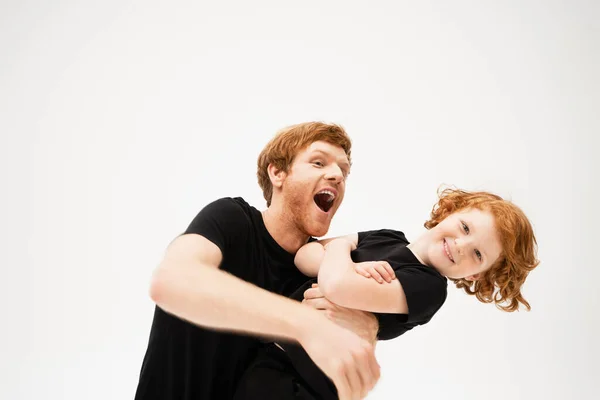 Excited man playing with redhead son crossing arms and smiling at camera isolated on grey — Stock Photo