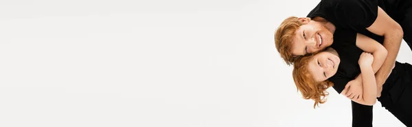 Cheerful young man embracing red haired son while having fun and smiling at camera isolated on grey, banner — Fotografia de Stock