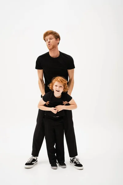 Full length of redhead man lifting cheerful son while having fun on light grey background — Stock Photo