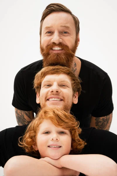 Cheerful red haired kid posing with crossed arms near father and bearded grandpa isolated on grey — Stock Photo
