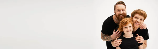 Family portrait of redhead boy with father and tattooed grandpa embracing isolated on grey, banner — Stock Photo