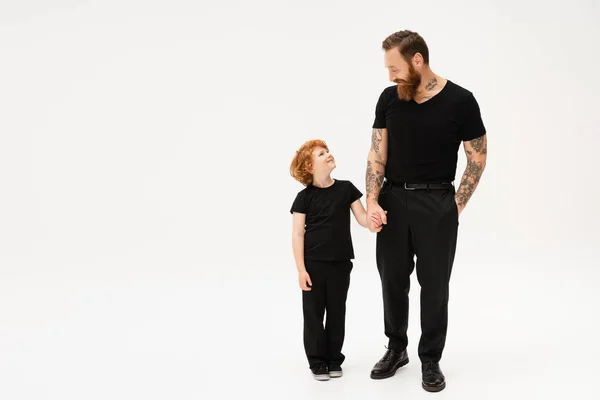 Full length of redhead boy with grandfather holding hands and looking at each other on light grey background — Stock Photo