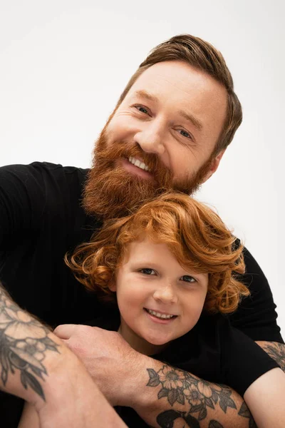 Family portrait of red haired boy with bearded tattooed grandpa smiling at camera isolated on grey — Stock Photo