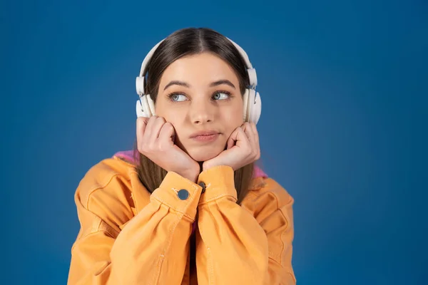 Pensive teenager in wireless headphones looking away isolated on blue — Stock Photo