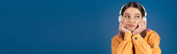 Thoughtful teenager in headphones looking away isolated on blue, banner — Stock Photo