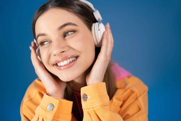 Portrait of joyful teenager in headphones looking away isolated on blue — Foto stock