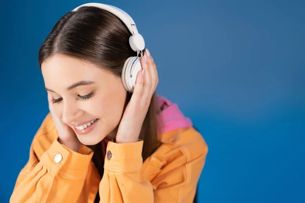 Pretty brunette teenager in headphones listening music isolated on blue — Stock Photo