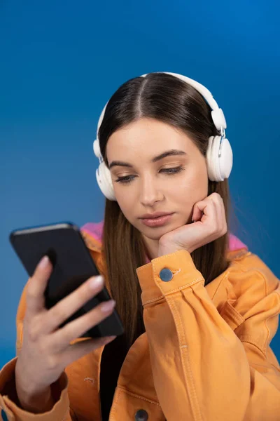 Teen girl in headphones using blurred smartphone isolated on blue — Fotografia de Stock