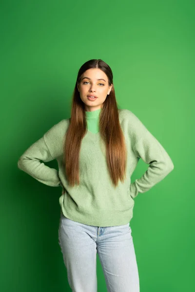 Pretty teen girl in jumper holding hands on hips on green background — Stock Photo