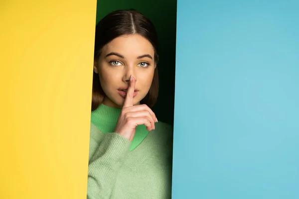 Brunette teen girl in jumper showing secret gesture on colorful background — Stock Photo