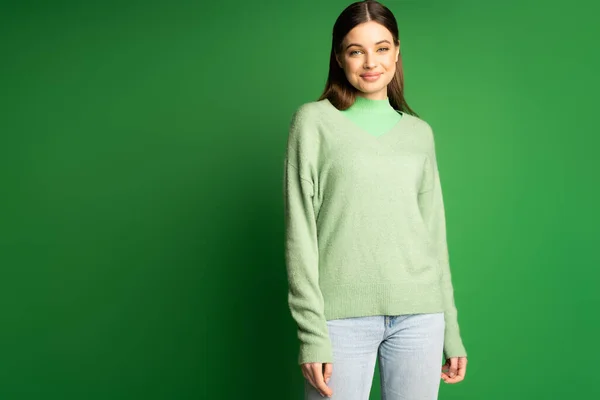 Positive teen girl in jumper and jeans standing on green background — Stock Photo