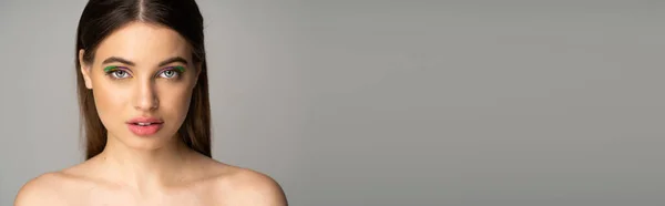 Гарненька брюнетка підліток з барвистим макіяжем стоїть ізольовано на сірому, банер — стокове фото