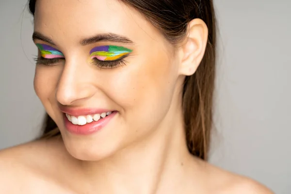 Happy teen model with colorful makeup smiling isolated on grey — Stock Photo