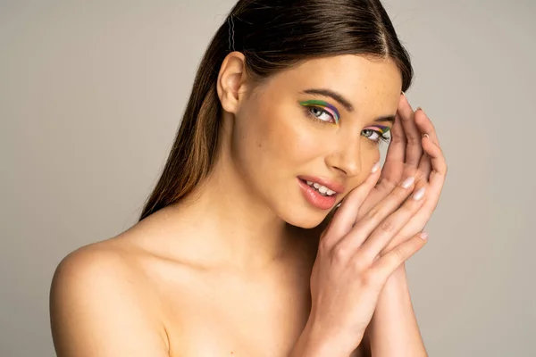 Smiling teen model with colorful makeup posing and looking at camera isolated on grey — Stock Photo