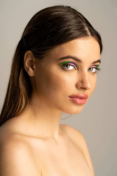 Teen model with naked shoulders and colorful eyeshadows looking at camera isolated on grey — Stock Photo