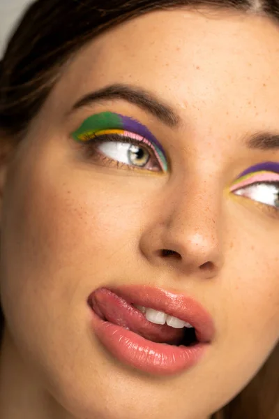 Cropped view of teen model with multicolored makeup sticking out tongue — Stock Photo