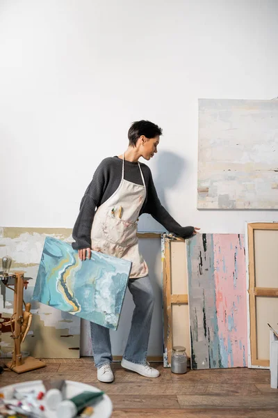 Side view of short haired artist holding paintings in studio — Stock Photo