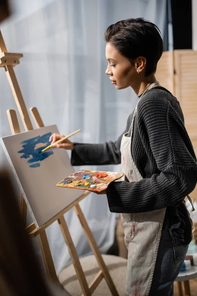 Side view of brunette artist painting on canvas in studio - foto de stock
