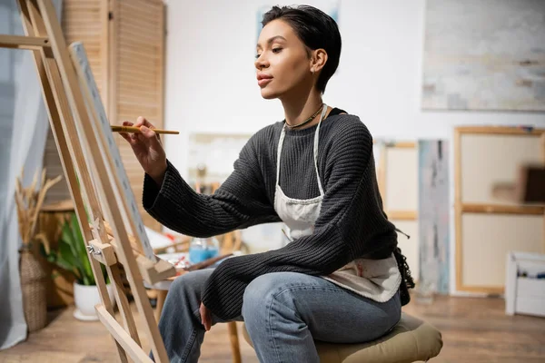 Short haired artist sitting and painting on canvas in studio — Fotografia de Stock