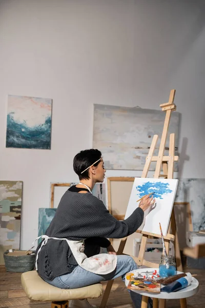 Side view of artist in apron painting on canvas in studio — Stock Photo