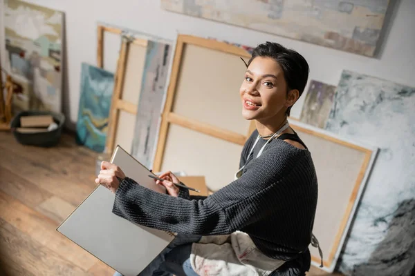 Young short haired artist holding pencil and sketchbook in studio — Stock Photo