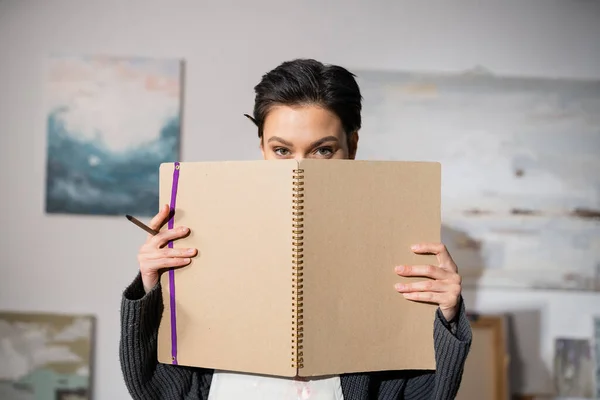 Short haired artist holding sketchbook near face in workshop — Stock Photo