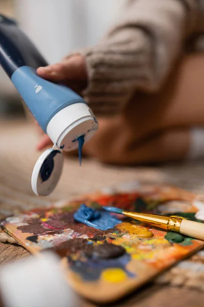 Cropped view of artist pouring paint on palette near paintbrush in workshop — Foto stock