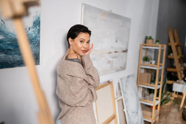 Sexy artist looking at camera near blurred drawings on wall — Stock Photo